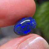 Blue speckled stone held between fingers with a blurred green background