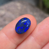 Blue fire opal stone held between fingers against a blurred background
