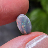 Opal stone held between fingers with a blurred natural background