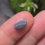 Opal stone held between fingers with a blurred green plant background
