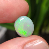 A polished green opal gemstone with a golden moss pattern, held in a person's hand.