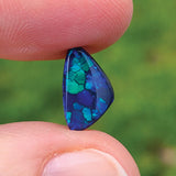 A person's hand holding a small, polished black opal gemstone with green and blue coloring.