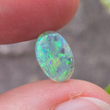 Opal stone held between fingers with a blurred natural background