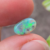 Opal stone held between fingers with a blurred natural background