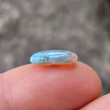 Opal stone held between fingers with a blurred natural background