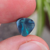 Blue green opal held between fingers with a blurred plant background