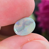 Opal stone held between fingers with a blurred purple flower in the background