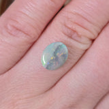 Opal stone held between fingers against a skin background