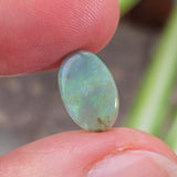Green gemstone held between fingers with a blurred natural background