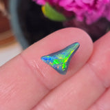 Triangular opal stone held between fingers with pink flowers in the background