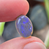 Person holding a blue opal stone between their fingers with a blurred background