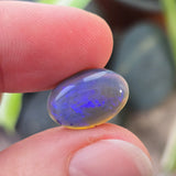 Person holding a blue and yellow gemstone between their fingers with a blurred background