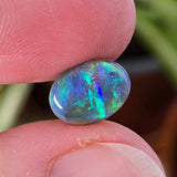 Opal stone held between fingers with a blurred natural background