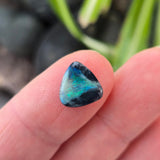 Teal gemstone held between fingers against a blurred natural background