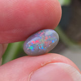 Opal stone held between fingers with a blurred natural background