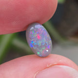 Opal stone held between fingers with a blurred natural background