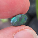 Opal stone held between fingers with a blurred natural background