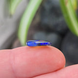 Small blue gemstone held between fingers with a blurred natural background