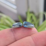 Free form shaped opals with green play of colour held between fingers against a blurred natural background