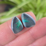 Free form shaped opals with green play of colour held between fingers against a blurred natural background