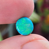 Blue opal stone held between two fingers with a blurred natural background