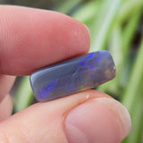 Hand holding a blue opal stone with a blurred plant background