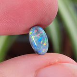Opal stone held between two fingers with a blurred green plant background