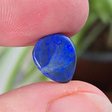 Blue stone held between two fingers with a blurred natural background