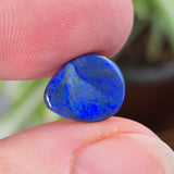 Blue gemstone held between fingers with a blurred plant background