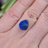 Blue gemstone held between fingers against a blurred natural background