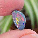Opal stone held between fingers with a blurred green plant background