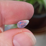 Small opal stone held between fingers with a blurred plant background
