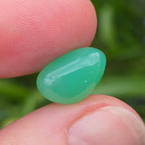 Green stone held between fingers with a blurred natural background