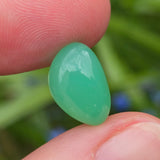 Green stone held between fingers with a blurred green background