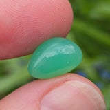 Green gemstone held between fingers with a blurred green background