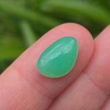 Green cat's eye gemstone on a finger with a blurred green background