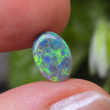 Opal stone held between two fingers with a blurred natural background
