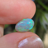 Opal stone held between two fingers with a blurred natural background