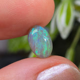 Opal stone held between fingers with a blurred natural background