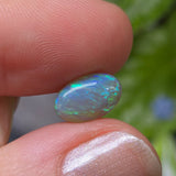 Opal stone held between fingers with a blurred natural background