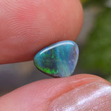 Opal stone held between fingers with a blurred natural background