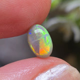 Opal stone held between two fingers with a blurred natural background