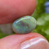 Opal stone held between fingers with a blurred natural background