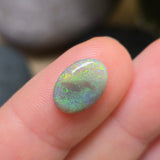Opal stone held between fingers with a blurred natural background
