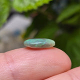 Greenish stone held between fingers with a blurred green background