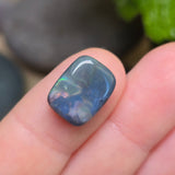Opal stone held between fingers with a blurred natural background