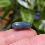 Blue stone held between fingers with a blurred natural background