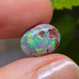 Opal stone held between fingers with a blurred green leaf background