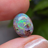 Opal stone held between fingers with a blurred green background