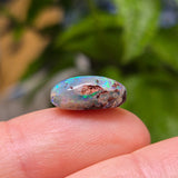 Opal stone held between fingers with a blurred natural background